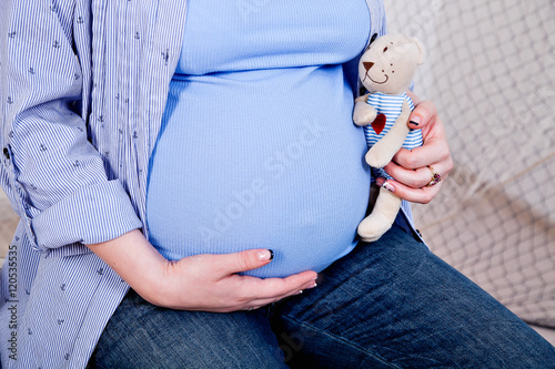 belly of a pregnant woman, a mother hands holding teddy bear