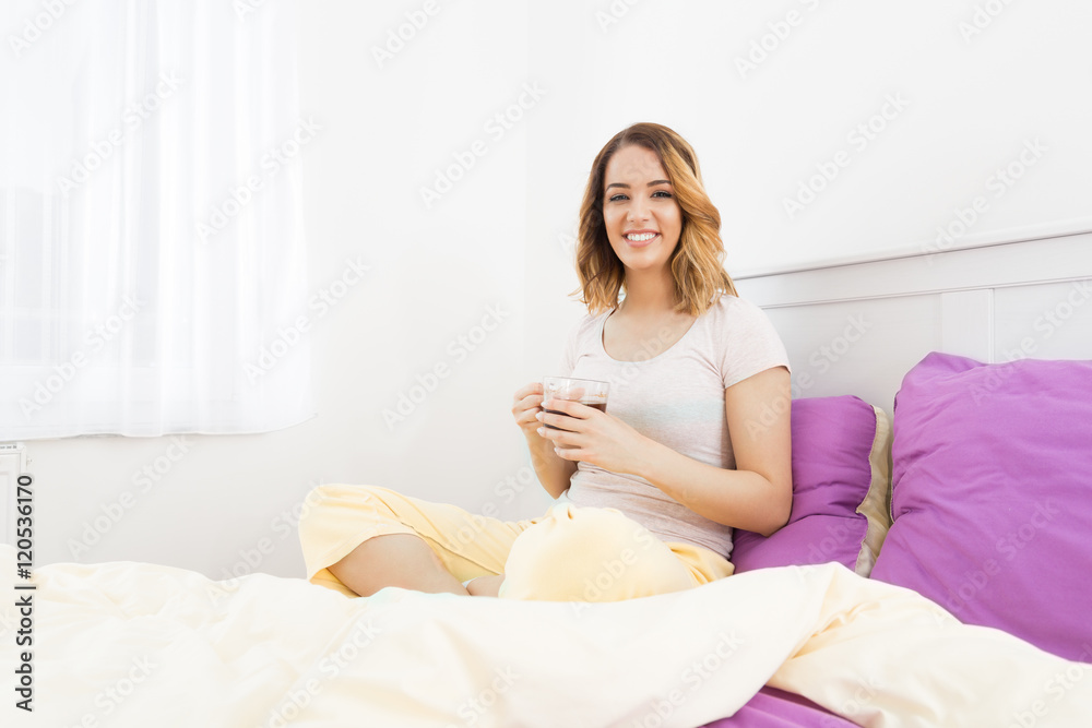 Beautiful young woman sitting on the bed in her bedroom and drinking coffee. Beautiful young woman sitting on the bed in her bedroom and drinking coffee.