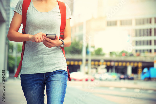 young woman walking with smart phone in modern city photo