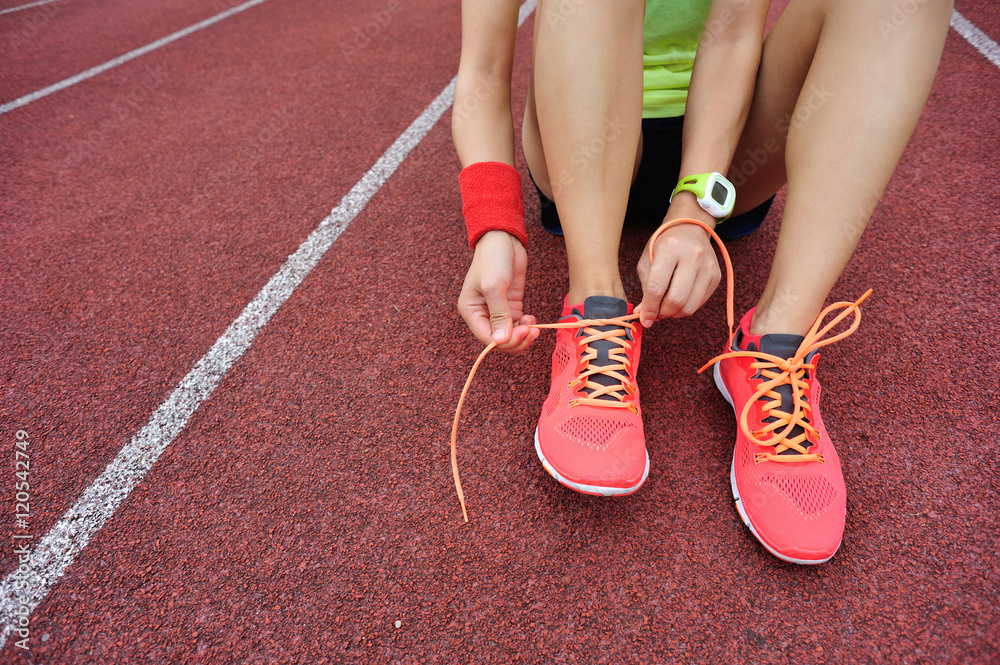 young woman runner tying shoelaces on tracks