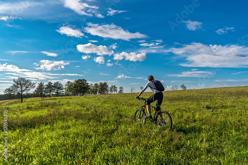 The girl rides a bicycle on green meadow