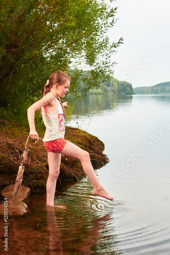 Little girl with an umbrella in cloudy day near the lake