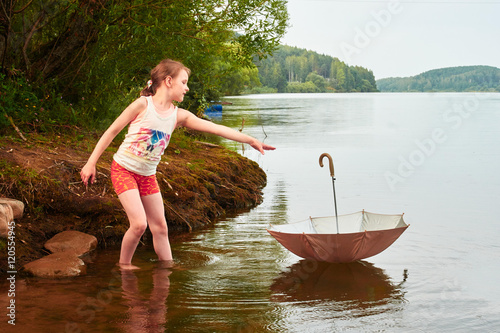Little girl lost her umbrella in cloudy day in the lake