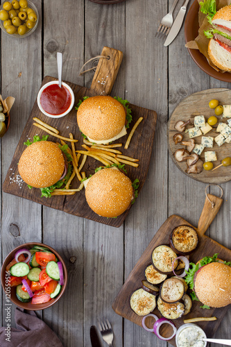 Different burgers with snacks on wooden table