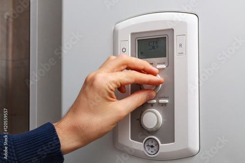 Men hand regulate temperature on 50 degree in control panel of central heating.