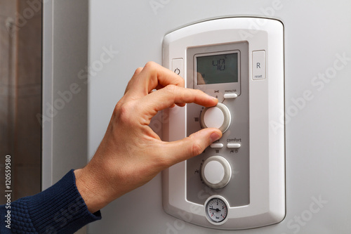 Men hand regulate low temperature on 40 degree in control panel of central heating.