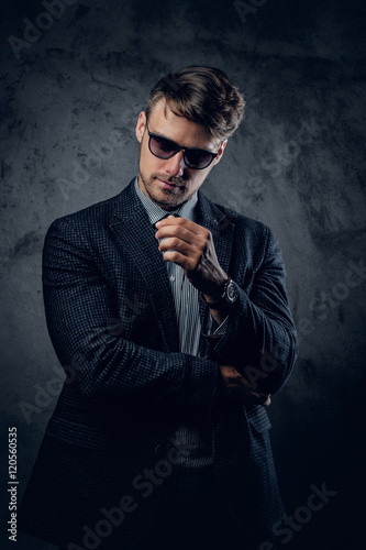 A man in a suit and sunglasses on grey background.