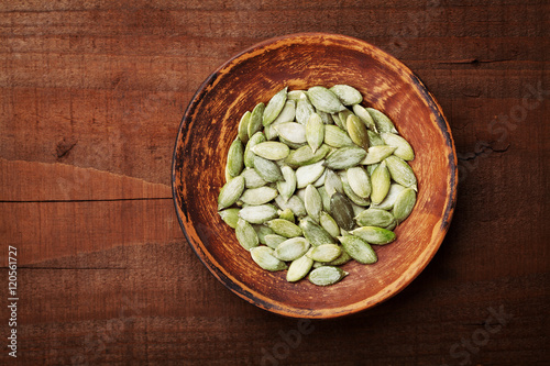 Pumpkin seeds in a clay bowl on rustic wooden background top view