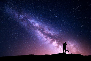 Milky Way. Night landscape with silhouettes of hugging and kissing man and woman on the mountain. Colorful sky with stars. Silhouette of lovers. Couple, relationship. Milky way with people. Universe