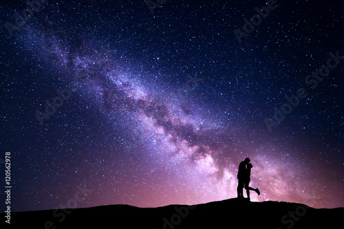 Milky Way. Night landscape with silhouettes of hugging and kissing man and woman on the mountain. Colorful sky with stars. Silhouette of lovers. Couple, relationship. Milky way with people. Universe