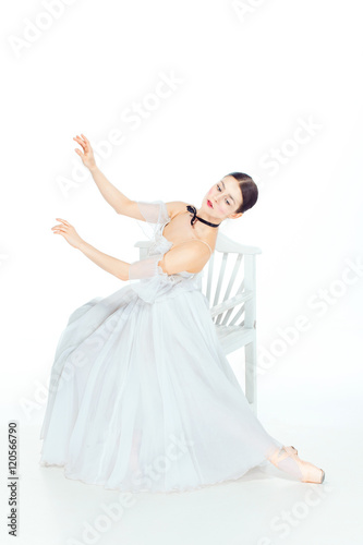 Ballerina in white dress sitting, studio background.