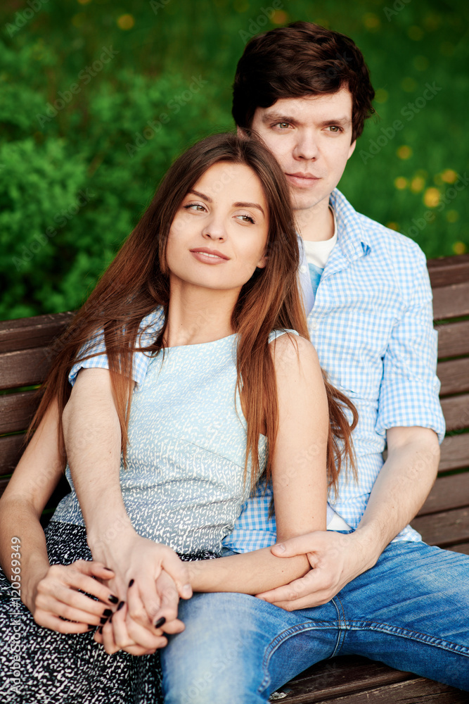Fototapeta premium Young couple sitting on a bench in the park in the summer and hugging
