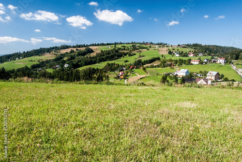 Tyniok hill above Koniakow village in Beskid Slaski mountains with meadows, isolated houses and blue sky with clouds photo