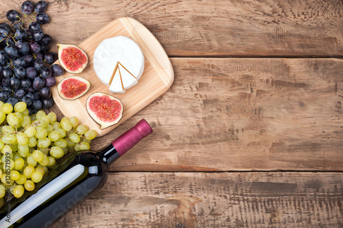 Bottle of red wine, grapes, cheese camambert and figs on old rustic wooden table. Food background. Top view