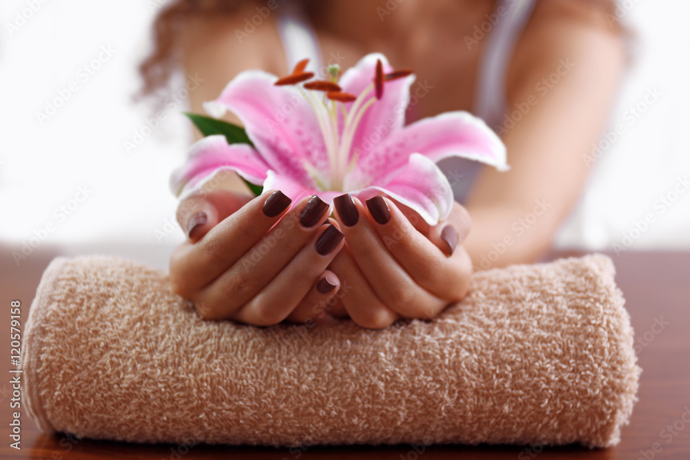 Female hands with brown manicure and pink lily on towel