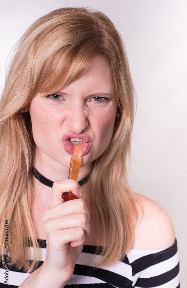 beautiful blonde woman is towing on a wine gum in her mouth beautiful blonde woman is towing on a wine gum in her mouth