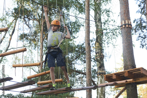 Portrait of active brave boy enjoying outbound climbing at adventure park on tree top