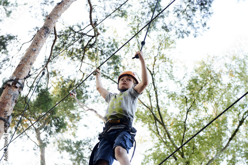 Portrait of active brave boy enjoying outbound climbing at adventure park on tree top © Petr Bonek