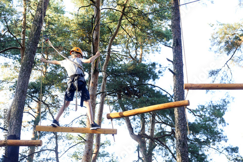 Portrait of active brave boy enjoying outbound climbing at adventure park on tree top