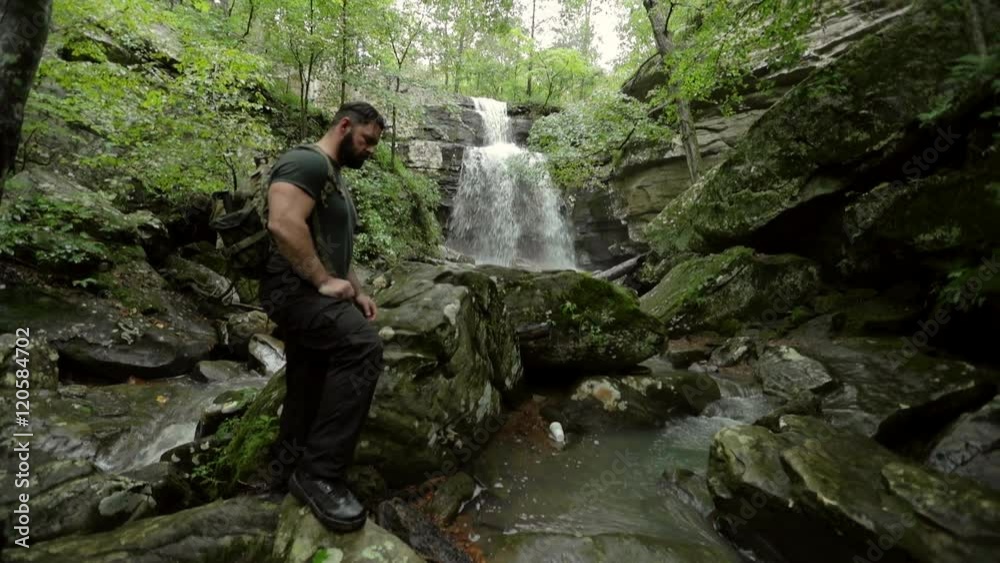 A male hiker stands at the bottom of Burden Falls, with a flowing creek at his feet. A male hiker stands at the bottom of Burden Falls, with a flowing creek at his feet.