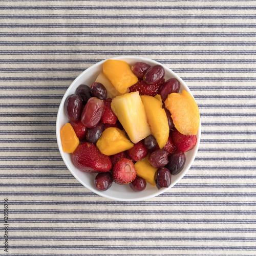 Mixed fruit in a bowl on a striped tablecloth top view.