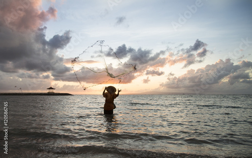 silhouette of a fisherman throwing a net in a water at sunrise in Bali photo