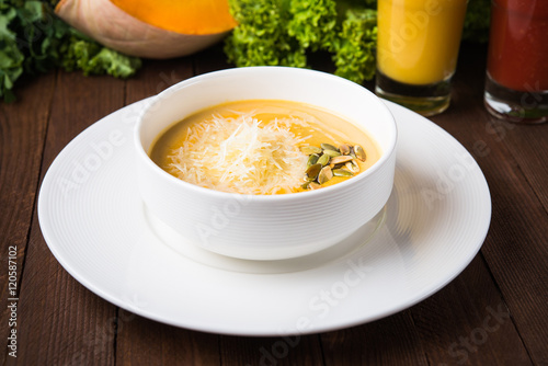 Creamy pumpkin soup with sids and parmesan on dark wooden background close up.