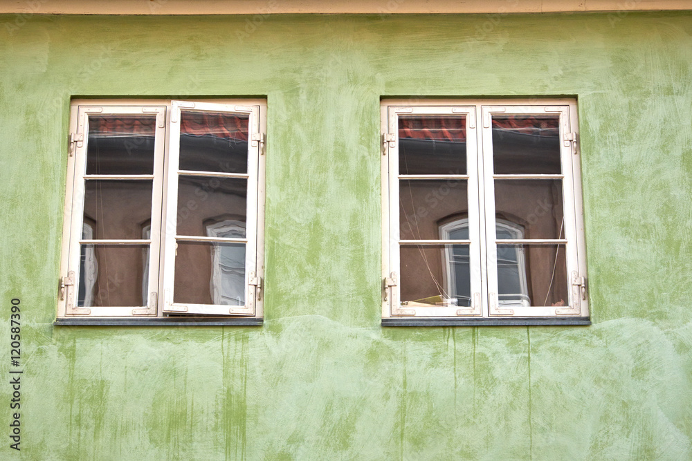 Two white painted danish colonial style windows fastened in a green plastered facade in Elsinore city, with reflections from an opposite old building