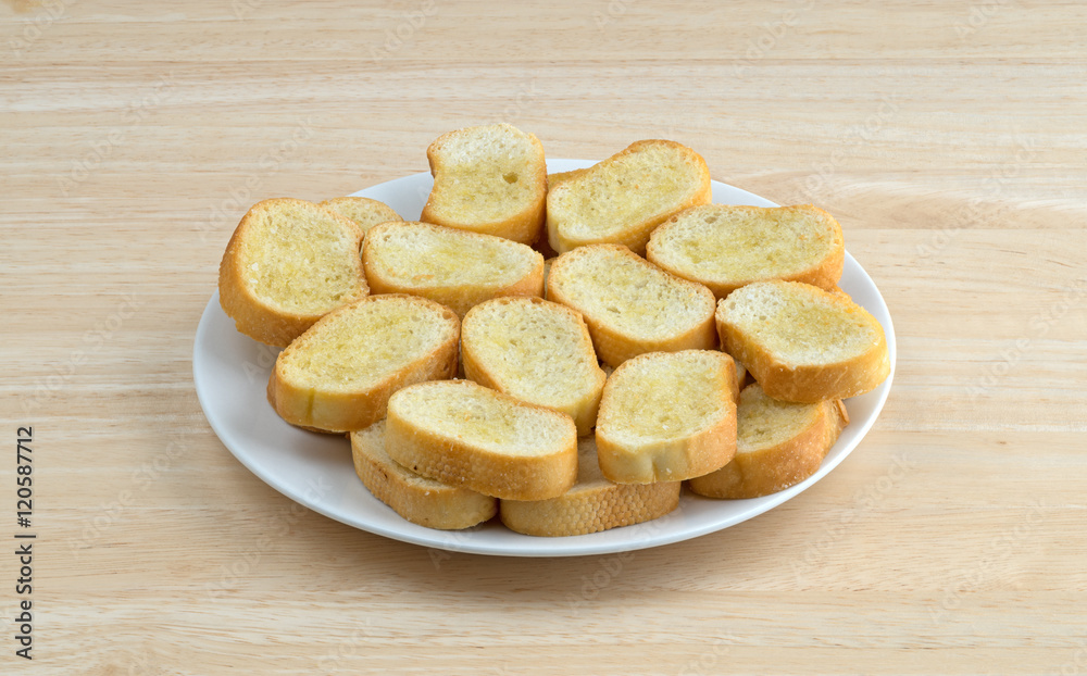 Crostini dabbed with olive oil on a plate atop a wood table.