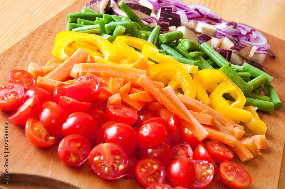 Cut vegetables arranged in rainbow colors on wooden cutting board Cut vegetables arranged in rainbow colors on wooden cutting board