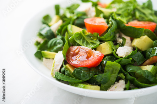 Fresh salad with chicken, tomatoes, spinach and avocado on white wooden background close up. Healthy food.