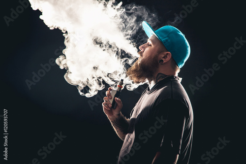 Men with beard  in sunglasses vaping and releases a cloud of vapor.