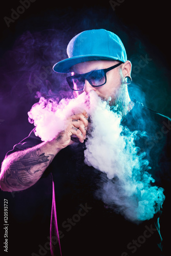 Men with beard in sunglasses vaping and releases a cloud of vapor.