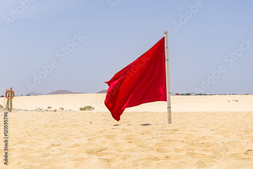 Red flag flying in the wind on the beach  photo taken in summer 2016 on Fuerteventura. Sunny day  as usual  no clouds on the sky and no people to see.