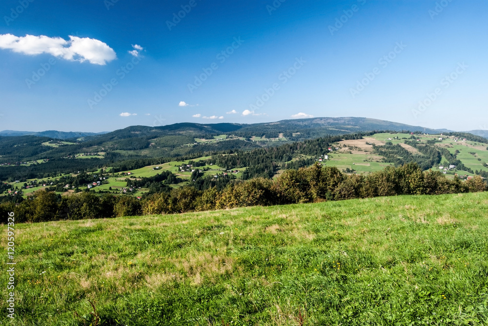 nice view from Ochodzita hill in Beskid Slaski mountains with hills, meadows, fields and settlement of Koniakow village during nice summer day with blue sky and clouds