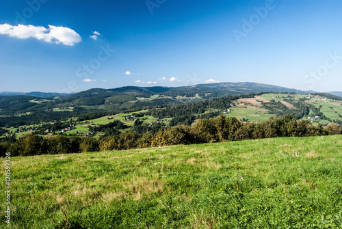 nice view from Ochodzita hill in Beskid Slaski mountains with hills, meadows, fields and settlement of Koniakow village during nice summer day with blue sky and clouds