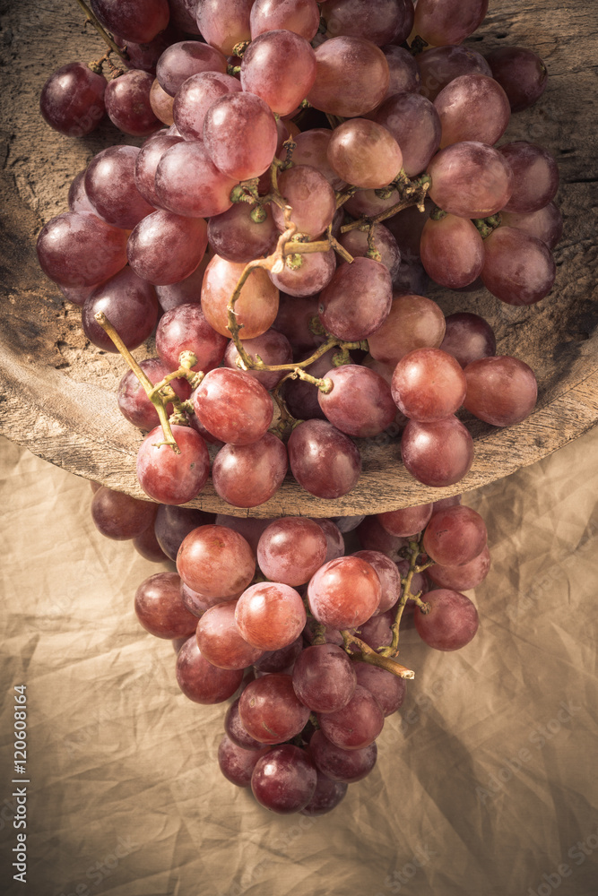 still life photography : red grapes bunch in old wooden bowl and on wrinkle tablecloth ( vintage color tone )