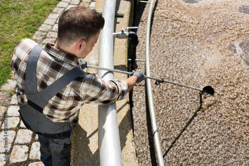 Worker taking water sample out of clarifier tank of sewage treatment plant