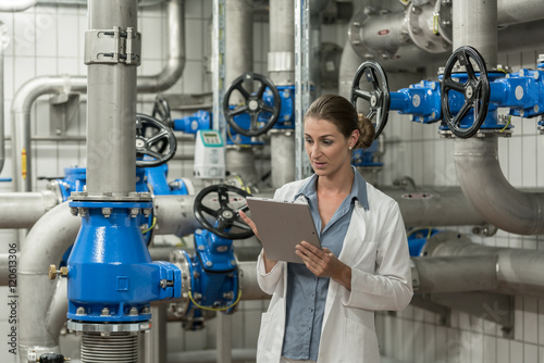 Laboratory technician checking report on tablet computer in pipe room of wastewater treatment plant