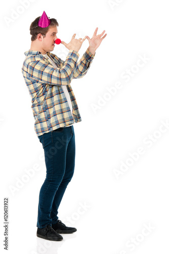 Handsome man clown isolated on white background. Teen boy with crazy look making faces and wearing red nose.