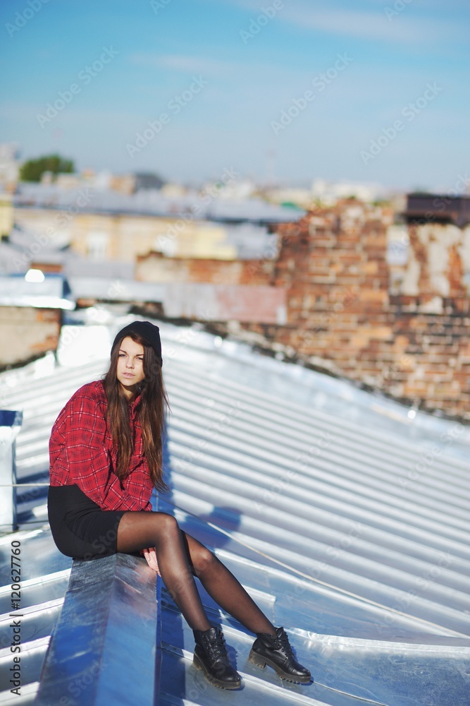 Portrait thoughtful courageous young girl sitting on the visor iron roof of high-rise buildings.