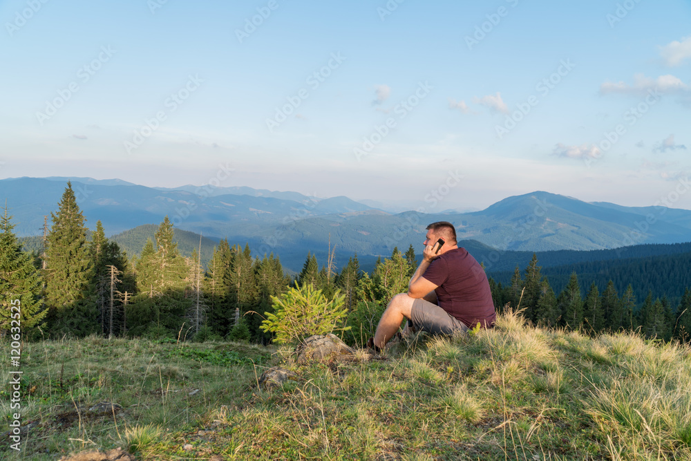 Man are sitting on a hill in mountains and talking on the phone