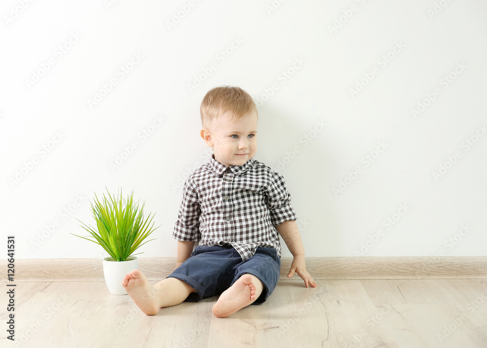 Fashionably dressed little boy with a flower in a pot sitting on a white wall background Fashionably dressed little boy with a flower in a pot sitting on a white wall background