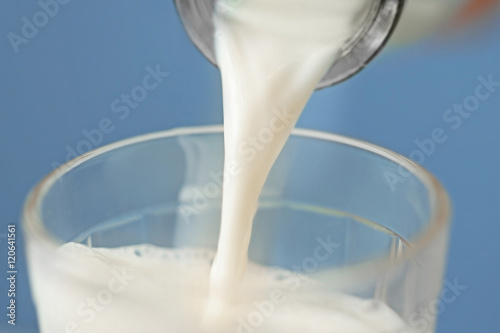 Milk pouring from a bottle into a glass on blue background, closeup