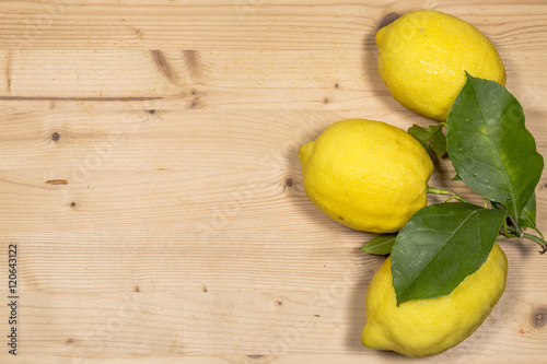 three lemons with leaves on wooden table