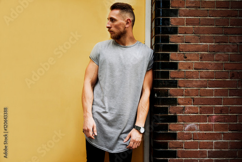 Attractive young muscular hipster wearing a gray T-shirt standing on a background of yellow wall. empty place for your logo o design. mock-up of blank t-shirt.