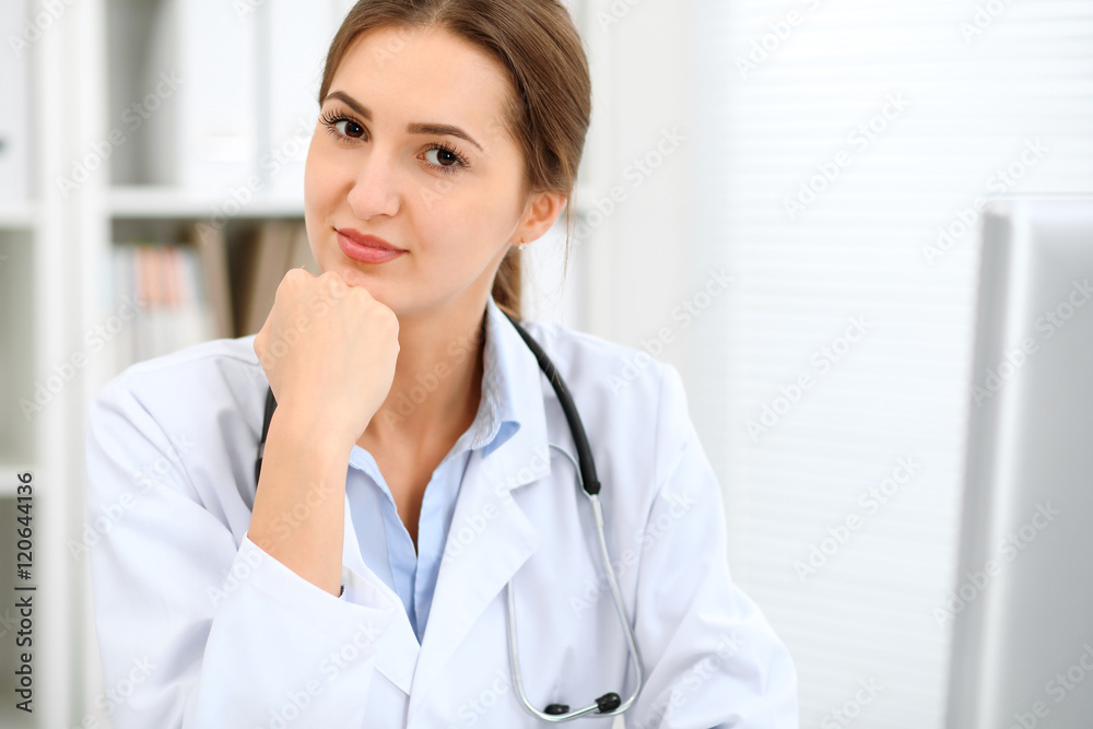 Young brunette female doctor sitting at the table and working at hospital office. Health care, insurance and help concept. Physician ready to examine patient Young brunette female doctor sitting at the table and working at hospital office. Health care, insurance and help concept. Physician ready to examine patient