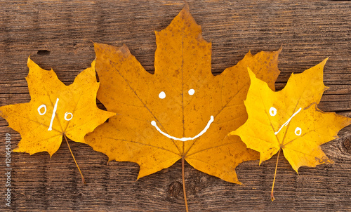Autumn leaves with smile on rustic wooden background. 