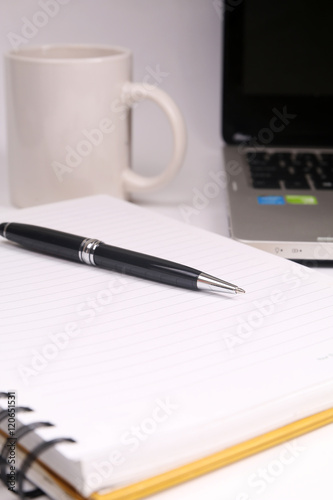 Pen on notebook with coffee mug and laptop 