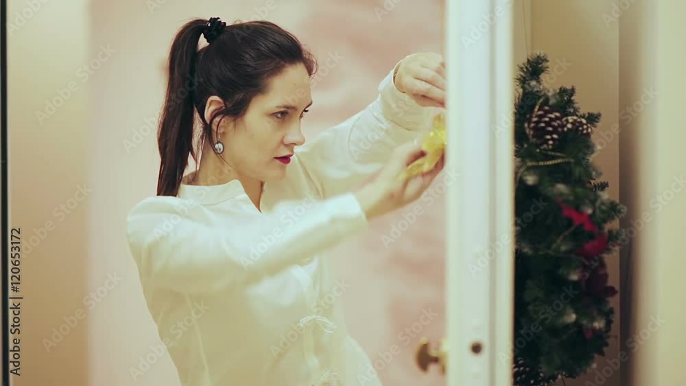 Young beautiful woman decorator hangs on the door a beautiful Christmas wreath Young beautiful woman decorator hangs on the door a beautiful Christmas wreath